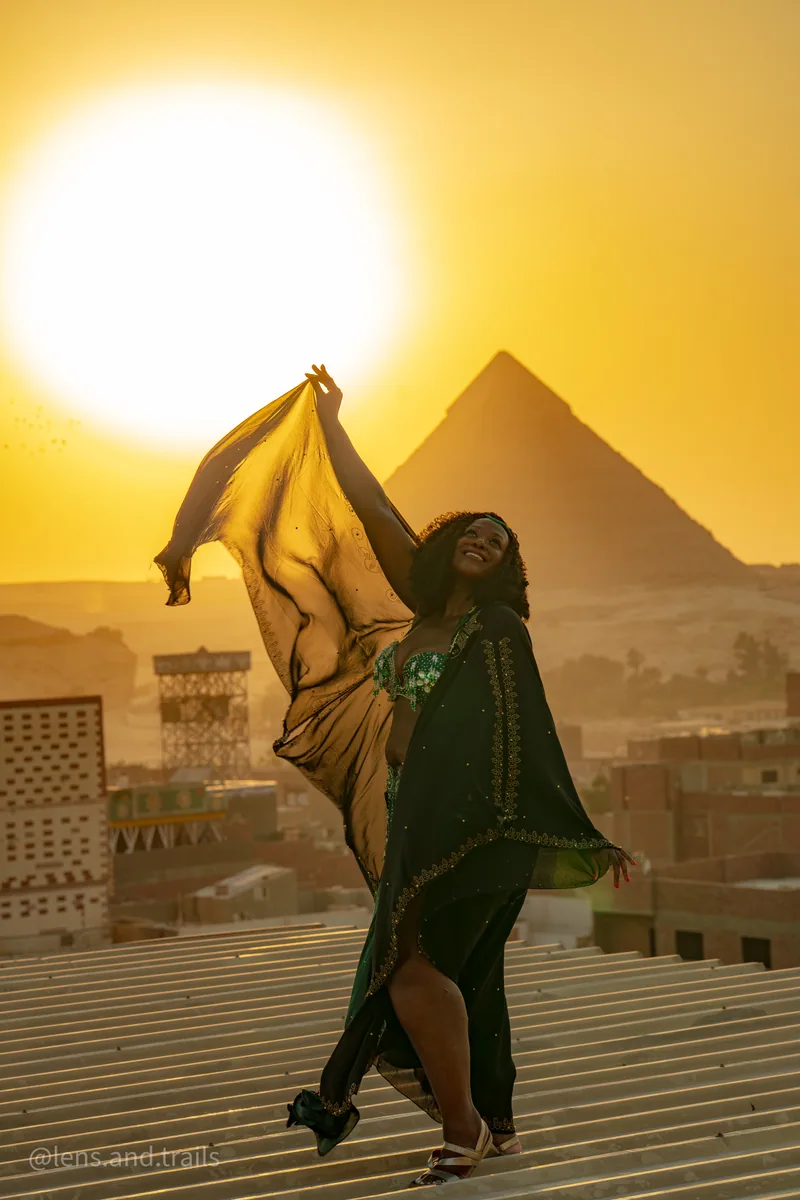 Taenzerin in Gruen-Gold mit riesiger Sonne hinter Pyramide